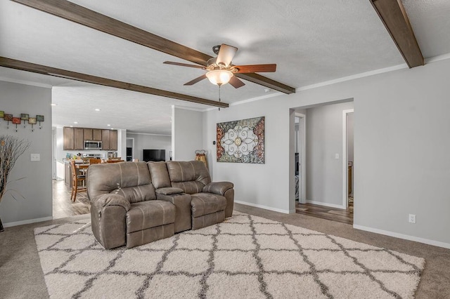 living room featuring beam ceiling, ceiling fan, crown molding, light colored carpet, and a textured ceiling