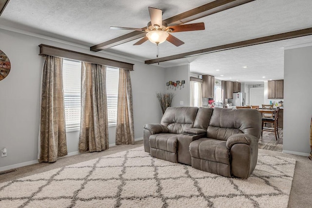 living room featuring beamed ceiling, ceiling fan, light colored carpet, and a textured ceiling