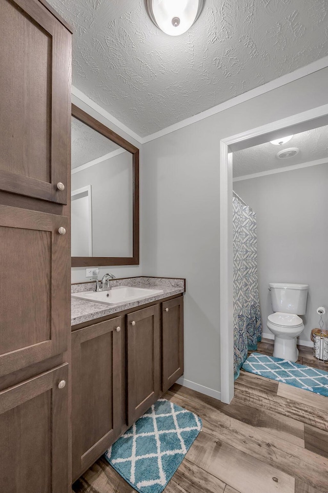 bathroom featuring crown molding, a textured ceiling, toilet, vanity, and hardwood / wood-style flooring