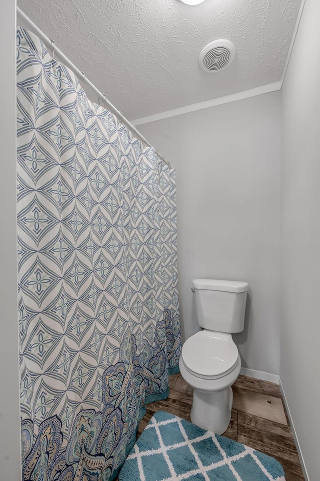 bathroom with a textured ceiling, toilet, wood-type flooring, and crown molding