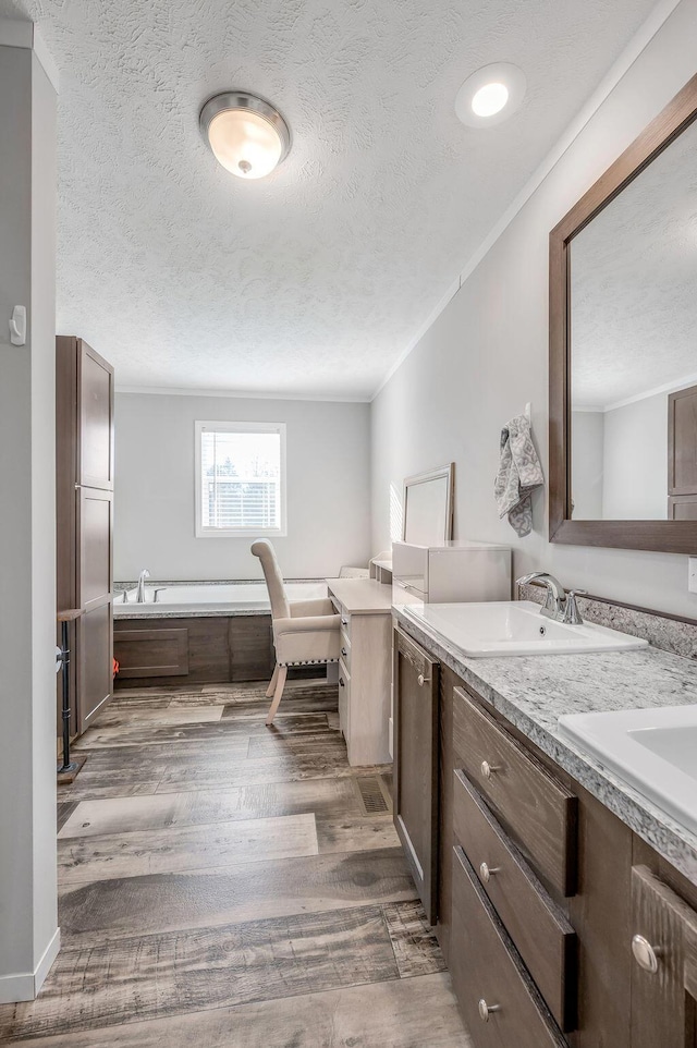 bathroom with a bath, crown molding, wood-type flooring, a textured ceiling, and vanity