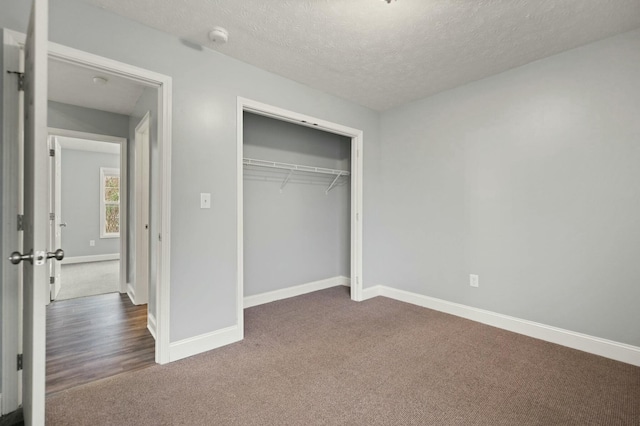 unfurnished bedroom featuring dark carpet, a textured ceiling, and a closet