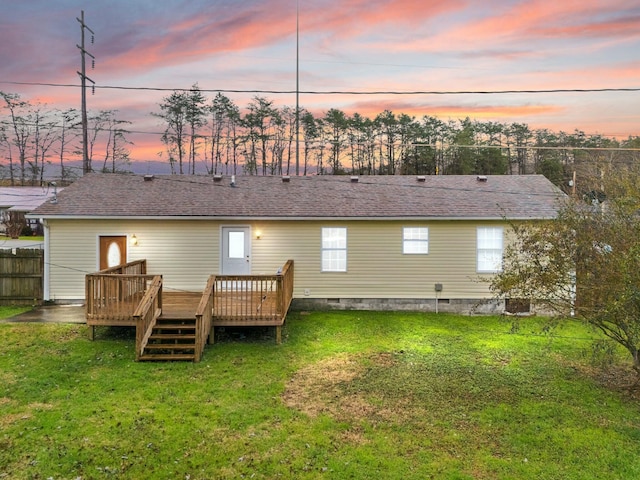 back house at dusk featuring a wooden deck and a yard