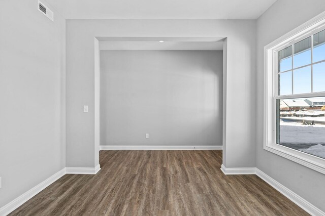 empty room featuring plenty of natural light, dark wood finished floors, visible vents, and baseboards