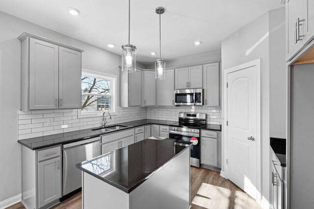 kitchen with dark wood-style flooring, stainless steel appliances, dark countertops, tasteful backsplash, and a sink