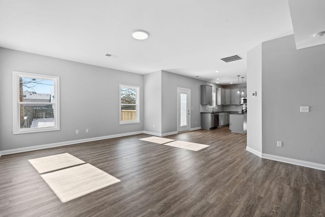 unfurnished living room with dark wood-type flooring, visible vents, and baseboards