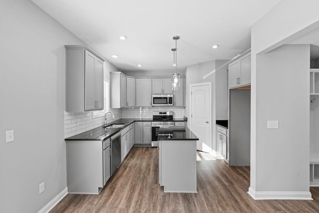 kitchen featuring decorative backsplash, appliances with stainless steel finishes, dark countertops, a sink, and a center island