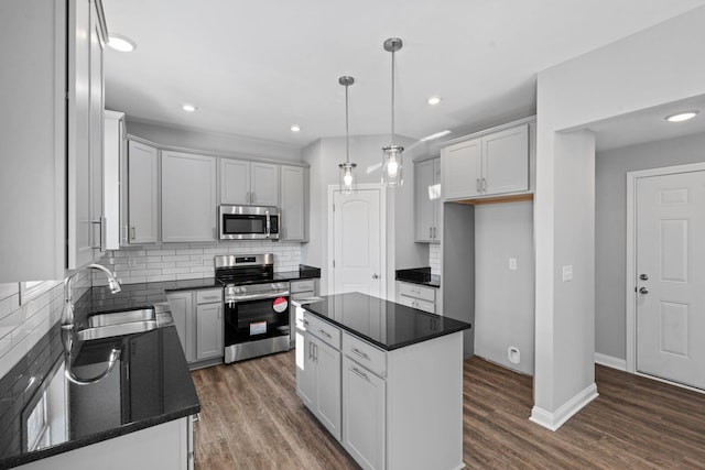 kitchen with a sink, appliances with stainless steel finishes, dark countertops, dark wood-style flooring, and backsplash
