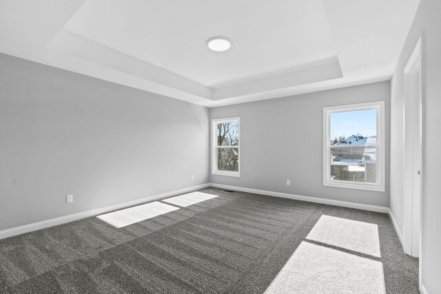 empty room with a raised ceiling, carpet flooring, visible vents, and baseboards