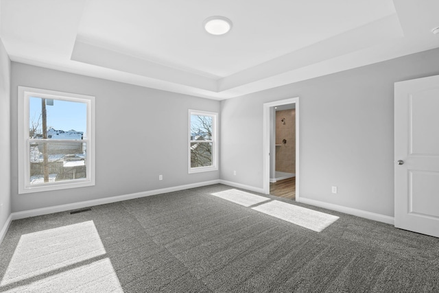 carpeted spare room with visible vents, a raised ceiling, and baseboards