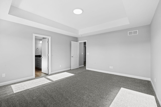 unfurnished bedroom featuring dark colored carpet, visible vents, a raised ceiling, and baseboards