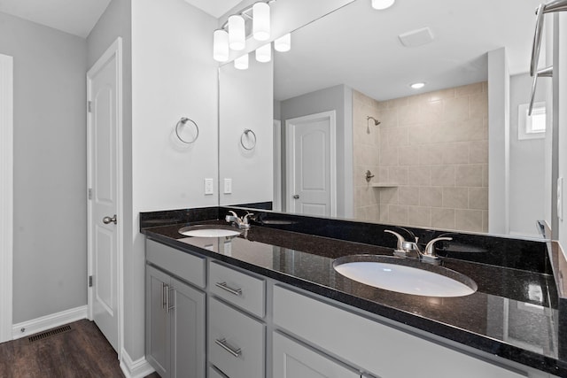bathroom featuring wood finished floors, visible vents, tiled shower, and a sink