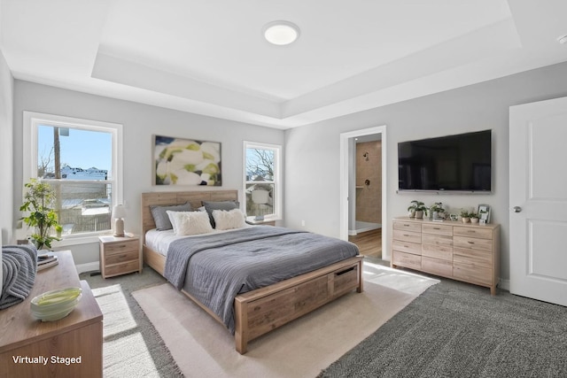 bedroom with ensuite bath, baseboards, light colored carpet, and a tray ceiling