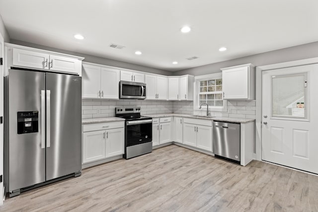 kitchen featuring white cabinets, appliances with stainless steel finishes, light stone counters, and sink