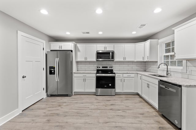 kitchen with light stone countertops, sink, stainless steel appliances, light hardwood / wood-style floors, and white cabinets