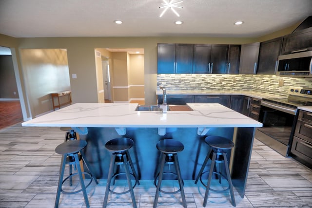 kitchen featuring light stone countertops, a breakfast bar, stainless steel appliances, sink, and an island with sink