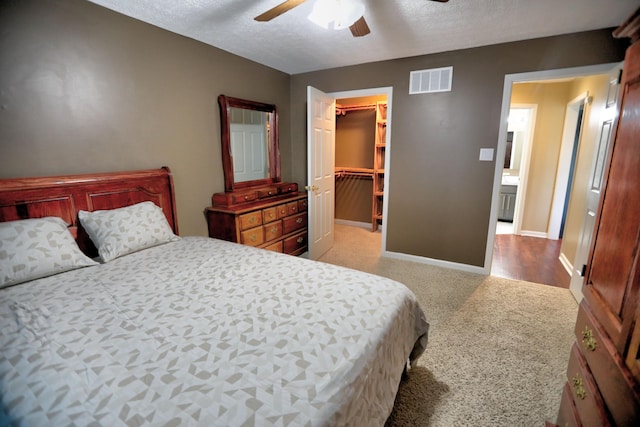 bedroom featuring light carpet, a walk in closet, ceiling fan, a textured ceiling, and a closet