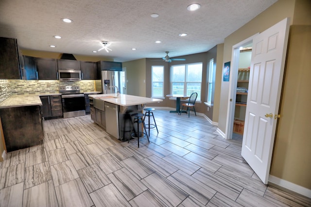 kitchen with ceiling fan, a center island, a textured ceiling, a kitchen bar, and appliances with stainless steel finishes