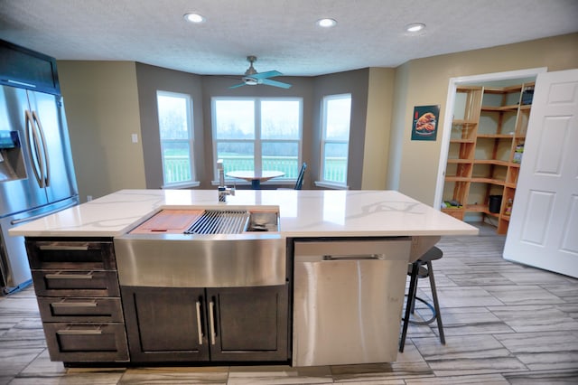 kitchen featuring ceiling fan, stainless steel fridge with ice dispenser, and a kitchen island with sink