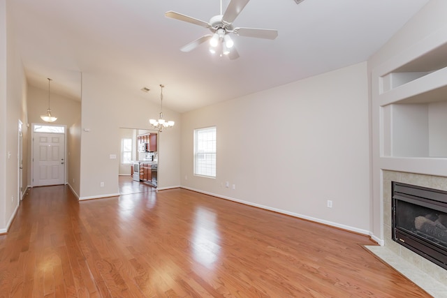 unfurnished living room with ceiling fan with notable chandelier, hardwood / wood-style flooring, lofted ceiling, and a tiled fireplace