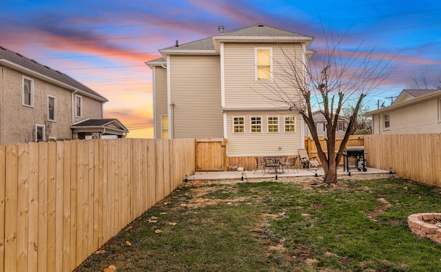 back house at dusk with a patio and a lawn