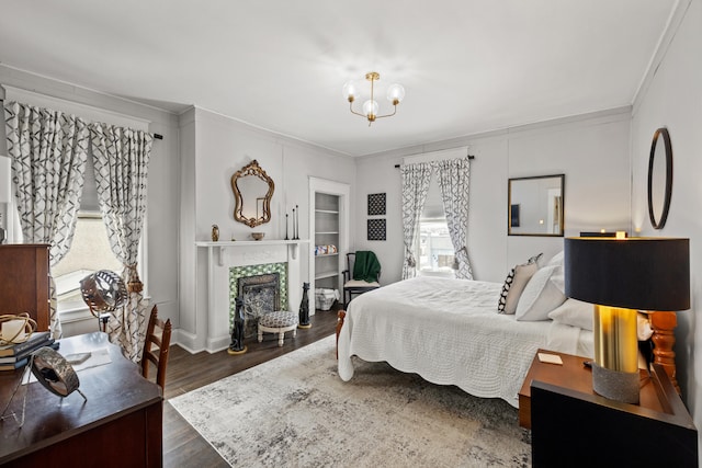 bedroom featuring dark hardwood / wood-style flooring, a tiled fireplace, crown molding, and a chandelier