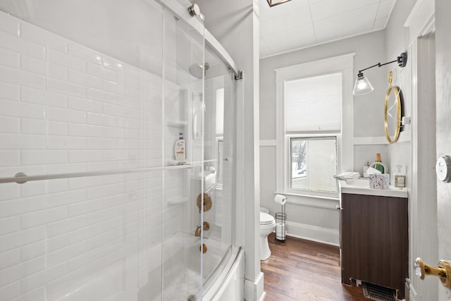 full bathroom featuring shower / bath combination with glass door, hardwood / wood-style floors, vanity, and toilet