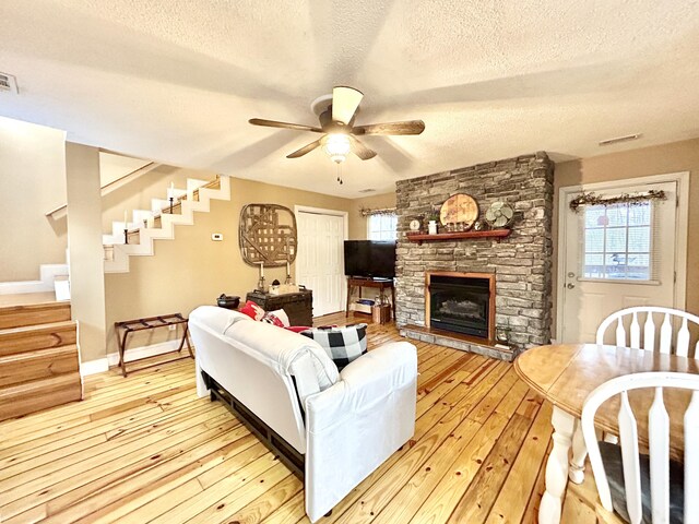 living room with ceiling fan, a fireplace, light wood-type flooring, and a textured ceiling