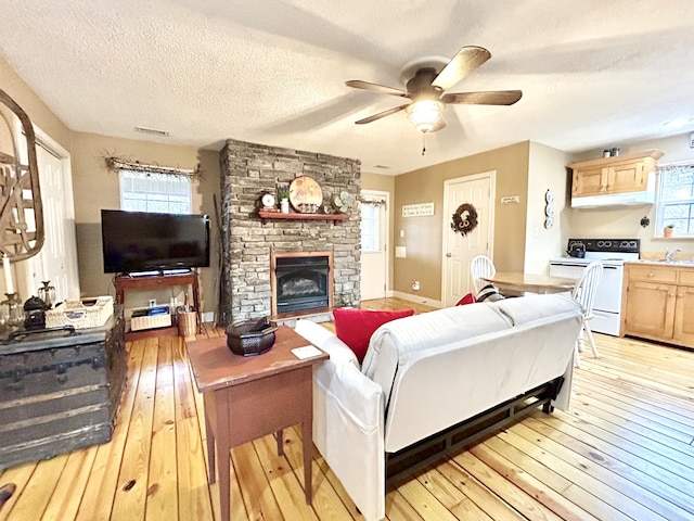 living room with a textured ceiling, ceiling fan, sink, a fireplace, and light hardwood / wood-style floors