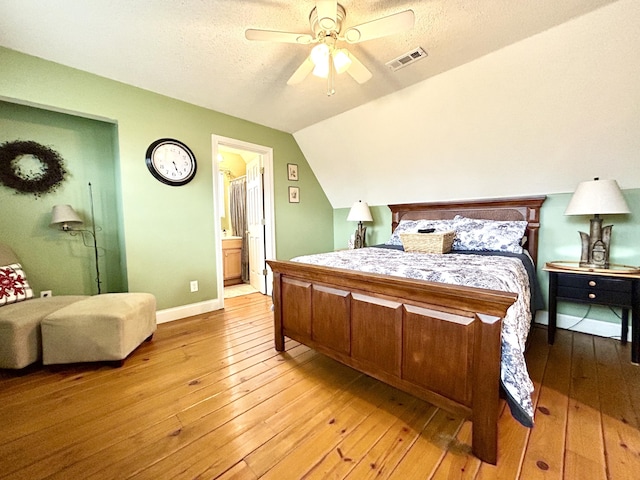 bedroom featuring ceiling fan, light hardwood / wood-style floors, ensuite bath, and vaulted ceiling