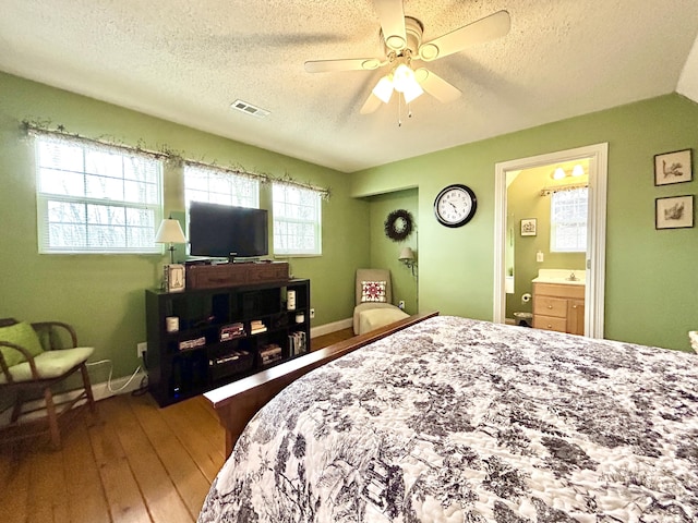 bedroom featuring a textured ceiling, hardwood / wood-style flooring, ensuite bath, and ceiling fan