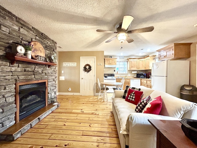 living room featuring a stone fireplace, ceiling fan, light hardwood / wood-style floors, and a textured ceiling