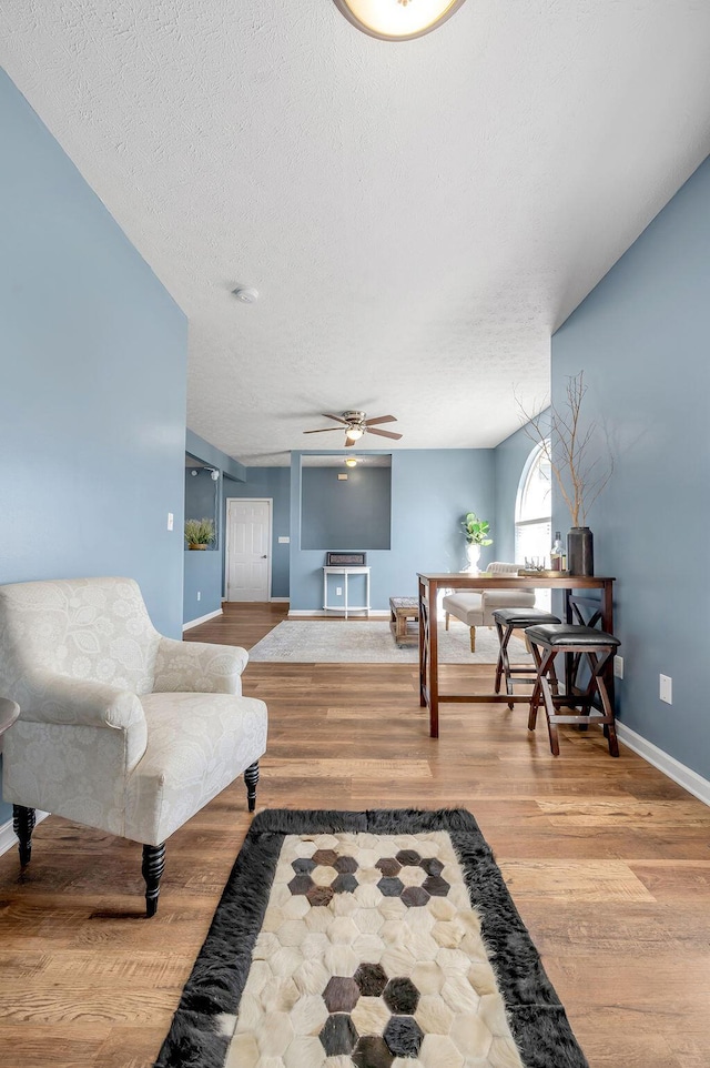 interior space featuring a ceiling fan, a textured ceiling, baseboards, and wood finished floors