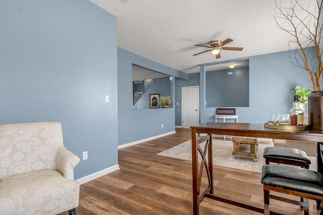 office area featuring a textured ceiling, wood finished floors, a ceiling fan, and baseboards