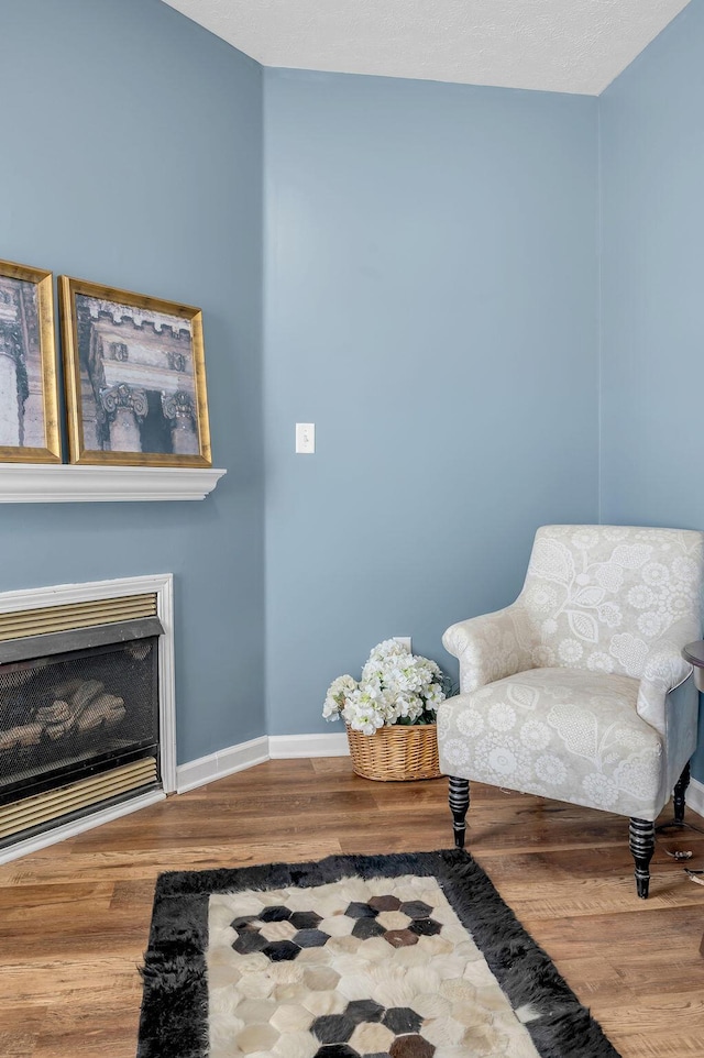 sitting room with a fireplace, wood finished floors, and baseboards