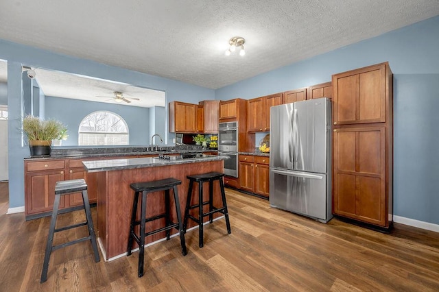 kitchen featuring stainless steel appliances, a breakfast bar area, dark countertops, and brown cabinets