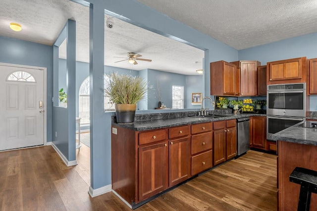 kitchen with brown cabinets, dark wood finished floors, stainless steel appliances, dark countertops, and a sink