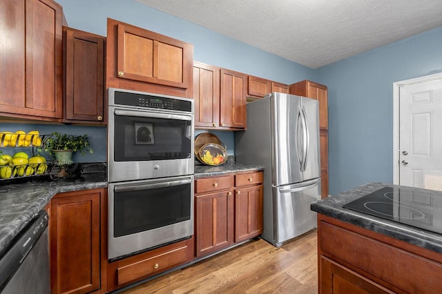 kitchen with appliances with stainless steel finishes, light wood-type flooring, brown cabinets, and a textured ceiling