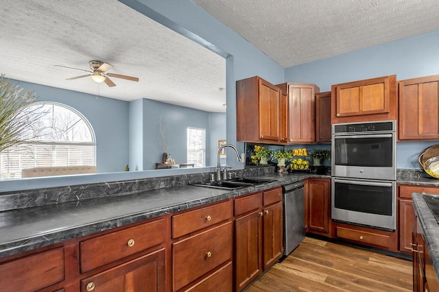 kitchen featuring appliances with stainless steel finishes, dark wood-type flooring, dark countertops, and a sink