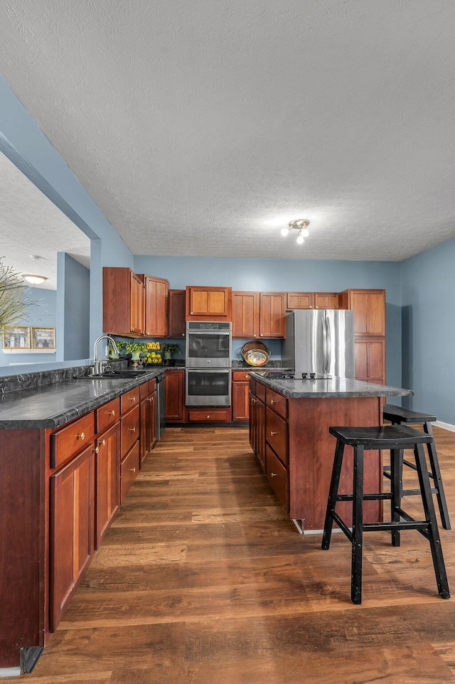 kitchen with dark countertops, dark wood-style floors, a kitchen island, stainless steel appliances, and a sink