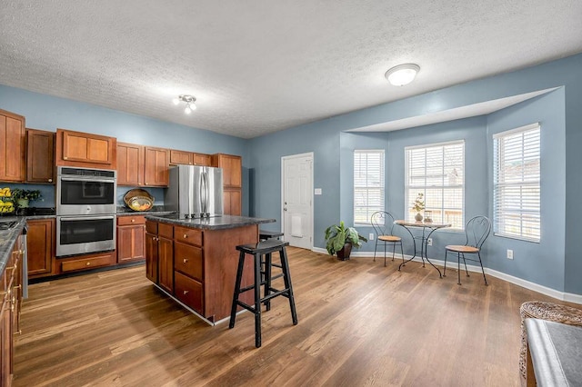 kitchen featuring dark wood-style floors, appliances with stainless steel finishes, brown cabinetry, a kitchen island, and baseboards