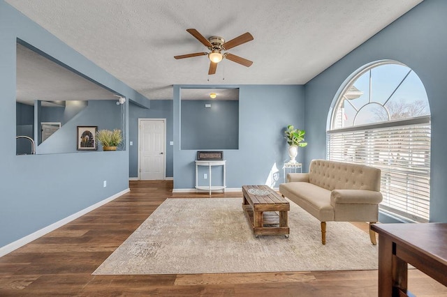 living room with a ceiling fan, a textured ceiling, baseboards, and dark wood-type flooring