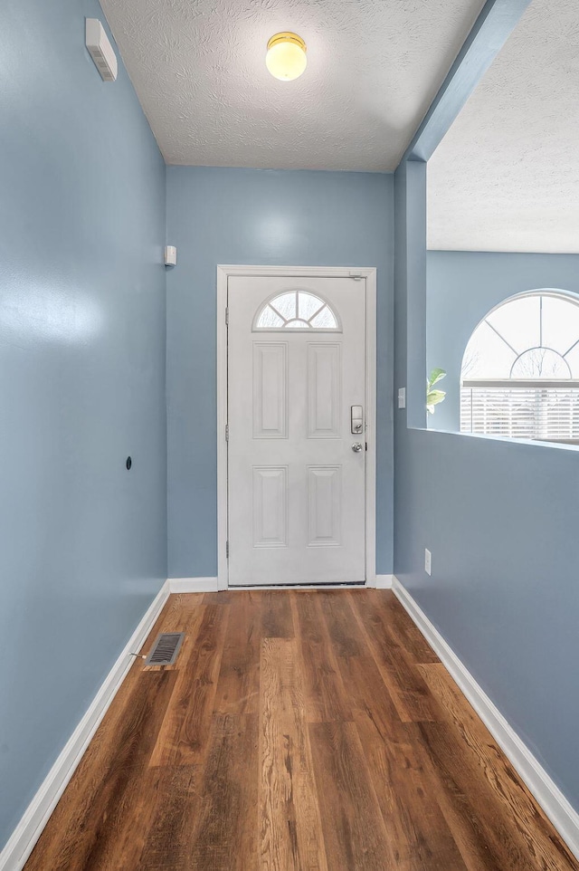 doorway featuring baseboards, a textured ceiling, visible vents, and dark wood-style flooring