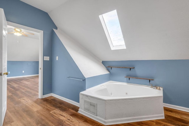 bathroom featuring ceiling fan, wood finished floors, vaulted ceiling with skylight, a whirlpool tub, and baseboards