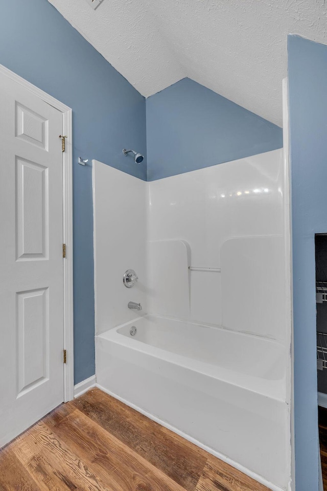 bathroom with lofted ceiling, tub / shower combination, a textured ceiling, and wood finished floors