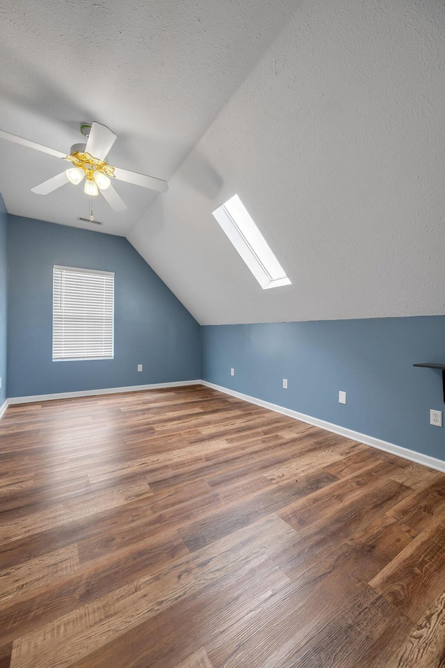 bonus room featuring lofted ceiling with skylight, a textured ceiling, baseboards, and wood finished floors