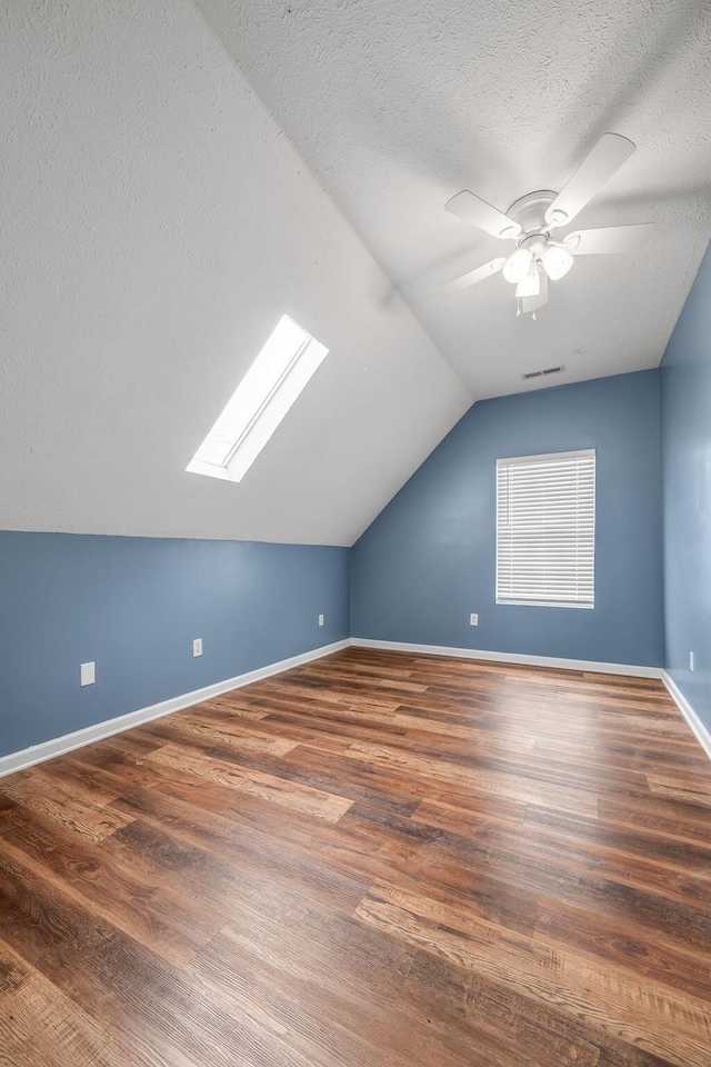 additional living space with dark wood-style floors, vaulted ceiling with skylight, baseboards, and a textured ceiling