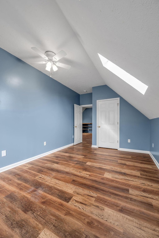 bonus room featuring baseboards, a ceiling fan, lofted ceiling with skylight, wood finished floors, and a textured ceiling