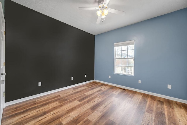 spare room featuring a ceiling fan, visible vents, baseboards, and wood finished floors