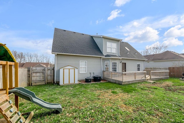 back of house with a lawn, a fenced backyard, roof with shingles, a shed, and a playground